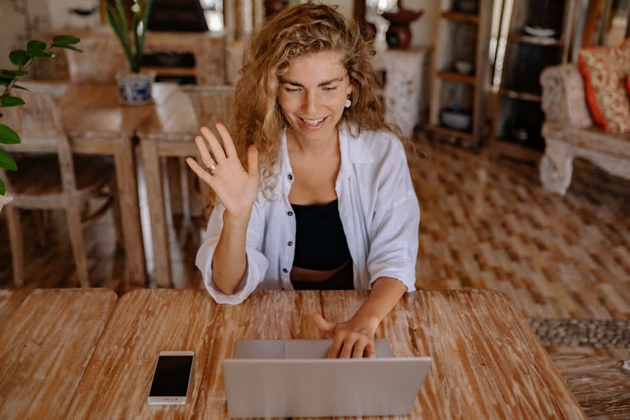 Woman smiling and waving during a virtual therapy video call from her home