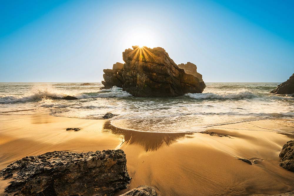 Sun shines through rock formation on a sandy beach