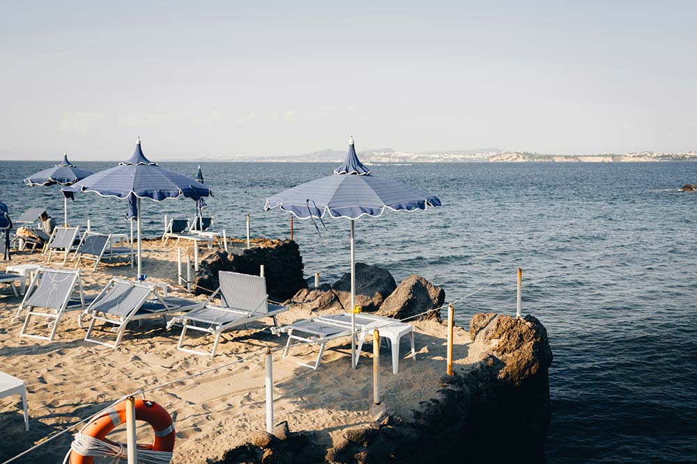 sandy beach with blue umbrellas, lounge chairs, and an ocean view
