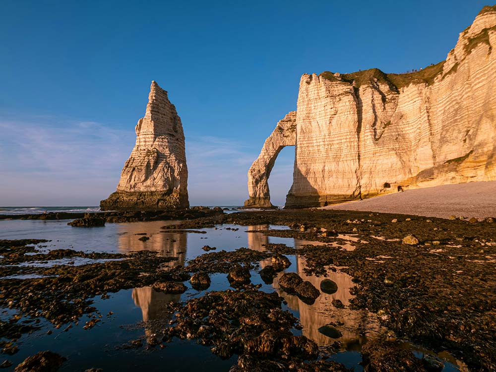 white cliffs, a natural arch, and a sea stack at sunset