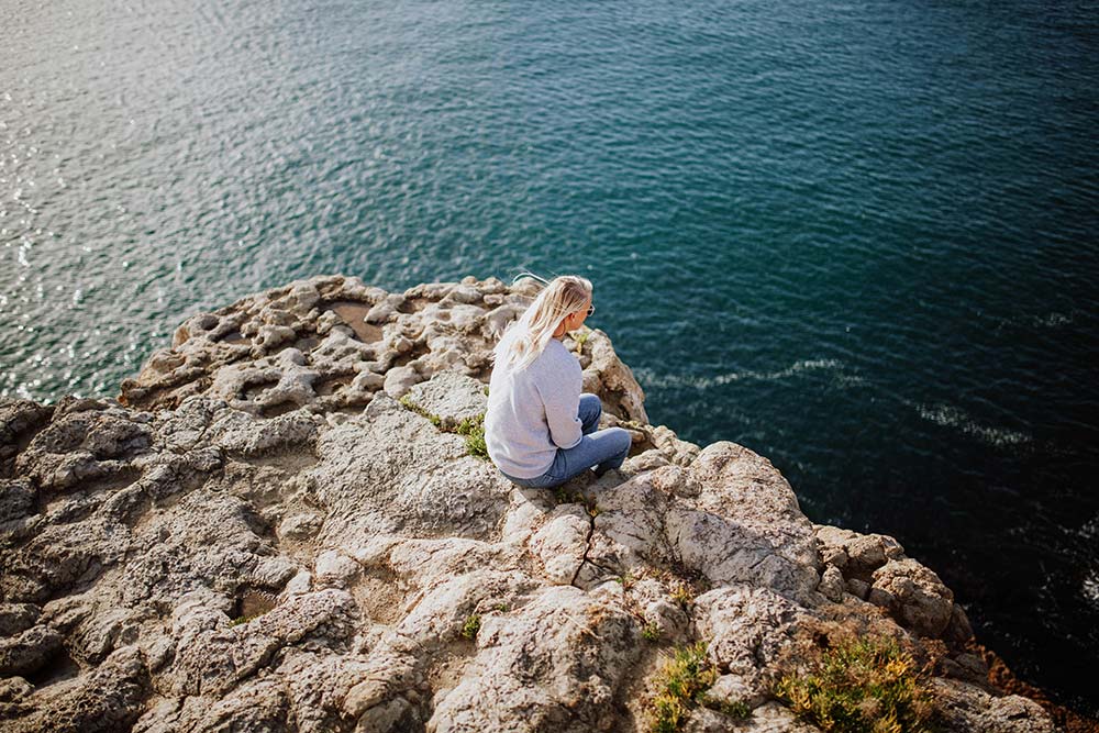 Woman sitting on a rock beside the ocean